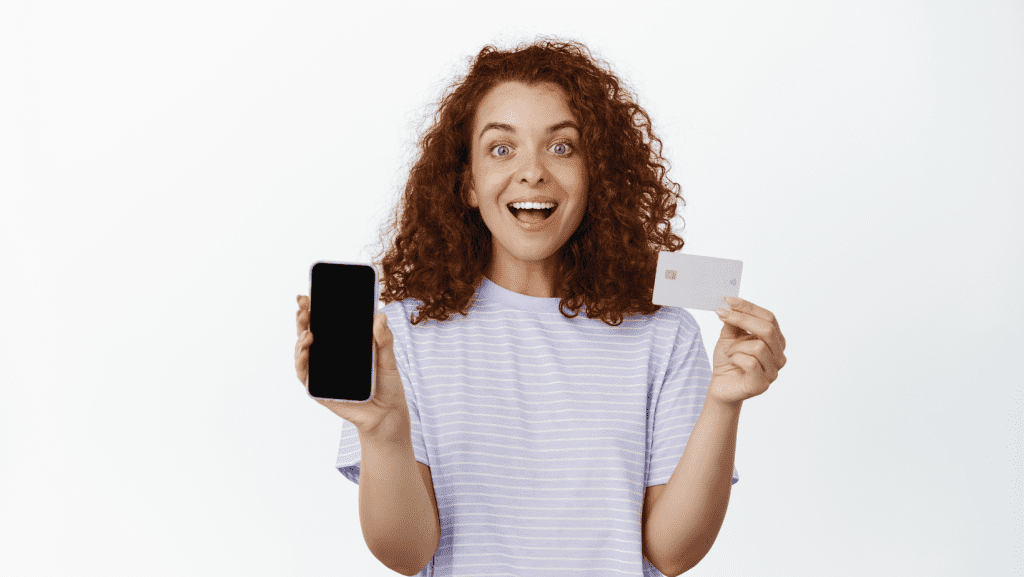 Mujer sonriendo sosteniendo su móvil y una tarjeta NFC de un comercio.