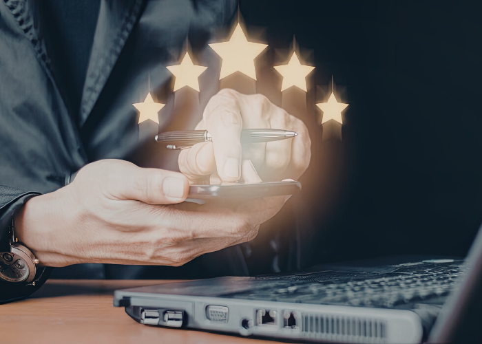 Une personne gérant des avis en ligne depuis un smartphone à côté d'un ordinateur portable, avec des icônes d'étoiles représentant l'automatisation et la centralisation des avis Google via wiReply